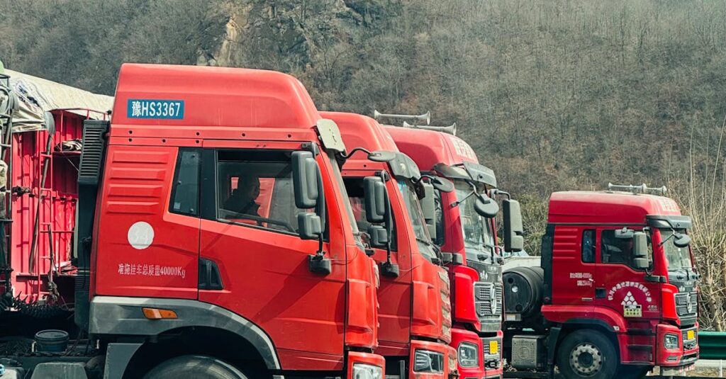 Array of red cargo trucks parked outdoors in a mountainous area during day.